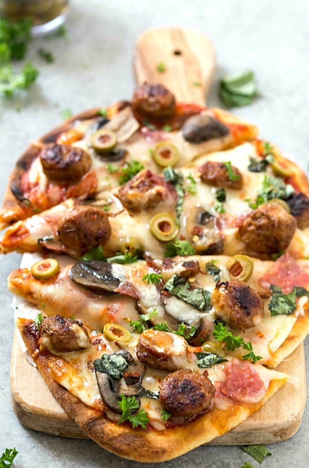 Easy Spicy Italian Sausage Grilled Flatbread Pizza - Crispy and Grilled naan flatbread layered with pizza sauce, shredded mozzarella cheese, hot Italian sausage, salami, manzanilla olives, mushrooms, and fresh basil! The perfect summer appetizer or main dish!