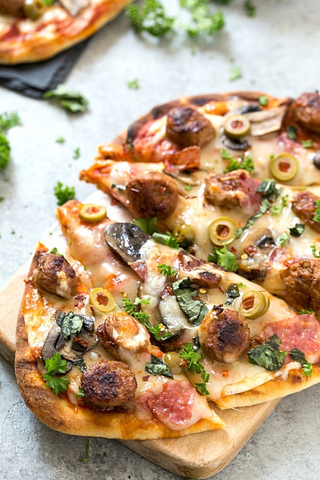 Easy Spicy Italian Sausage Grilled Flatbread Pizza - Crispy and Grilled naan flatbread layered with pizza sauce, shredded mozzarella cheese, hot Italian sausage, salami, manzanilla olives, mushrooms, and fresh basil! The perfect summer appetizer or main dish!