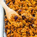 Homemade pumpkin granola on a baking sheet with a wooden spoon