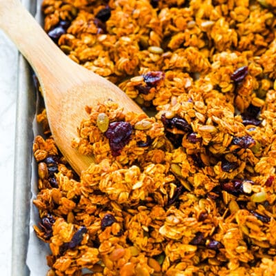 Homemade pumpkin granola on a baking sheet with a wooden spoon