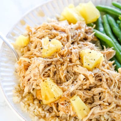 Small plate containing shredded chicken with a homemade teriyaki sauce over the top with pineapple chunks and green beans on the side