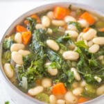 looking down on a bowl of soup with white beans, carrots, and kale