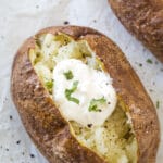 Looking down on a cooked baked potato topped with sour cream, salt, pepper, and parsley