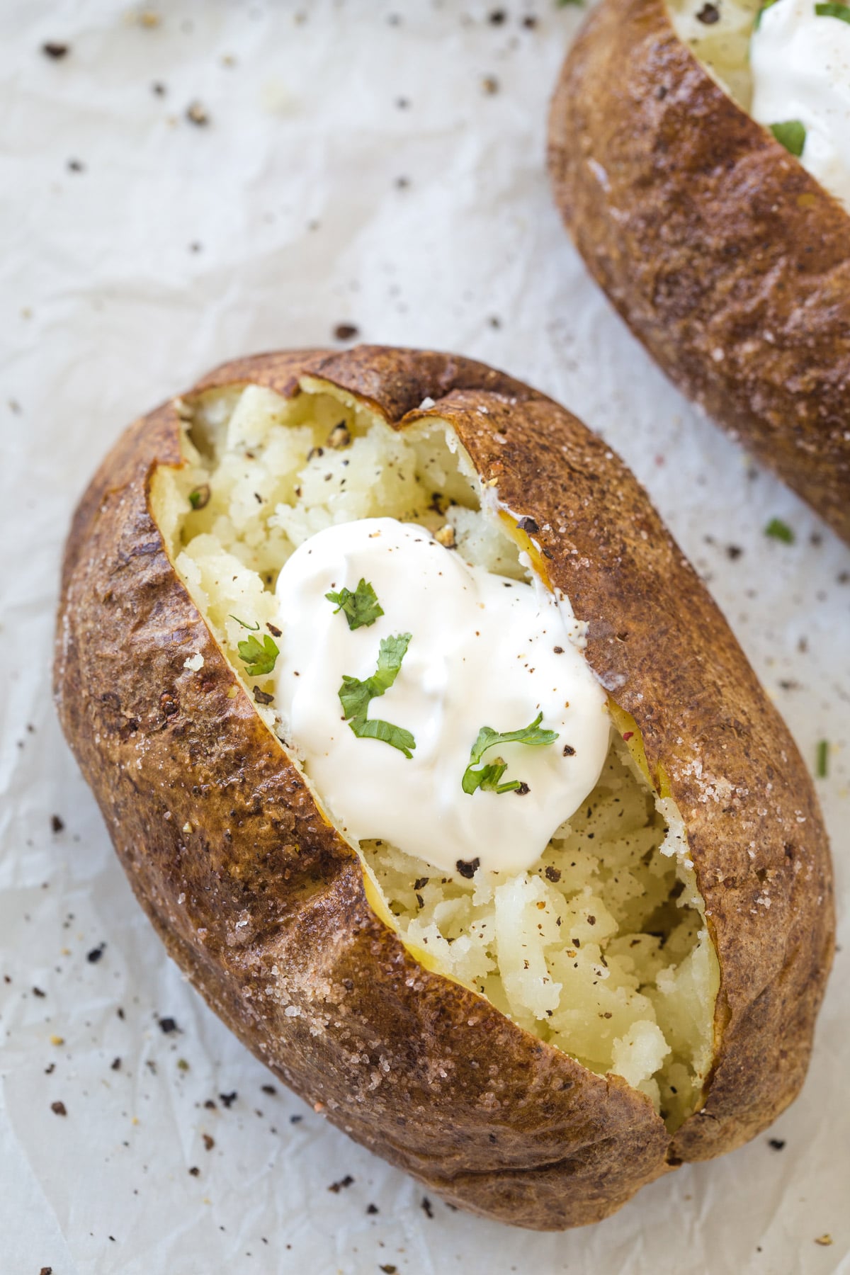 Looking down on a cooked baked potato topped with sour cream, salt, pepper, and parsley