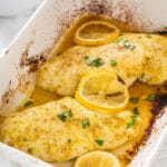 Closeup of lemon pepper chicken breasts on a casserole dish topped with lemon slices and fresh parsley