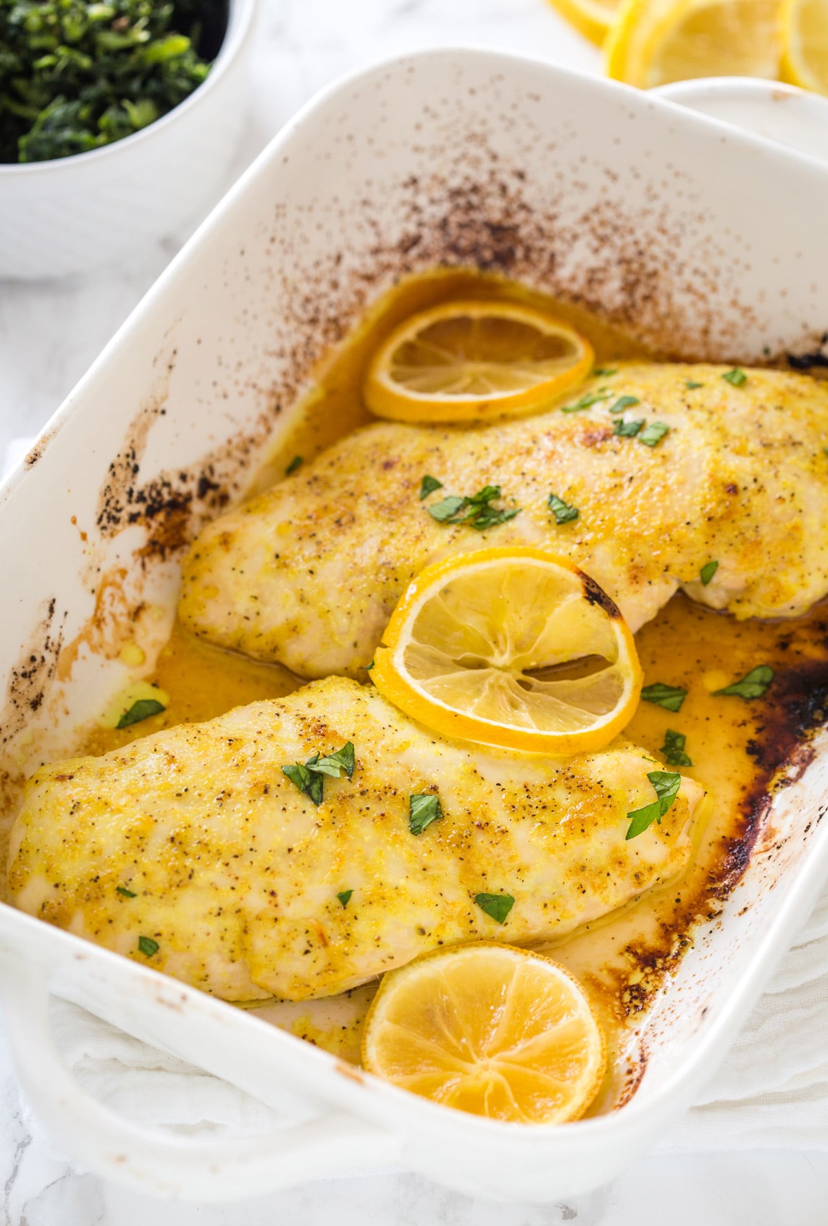 Closeup of lemon pepper chicken breasts on a casserole dish topped with lemon slices and fresh parsley