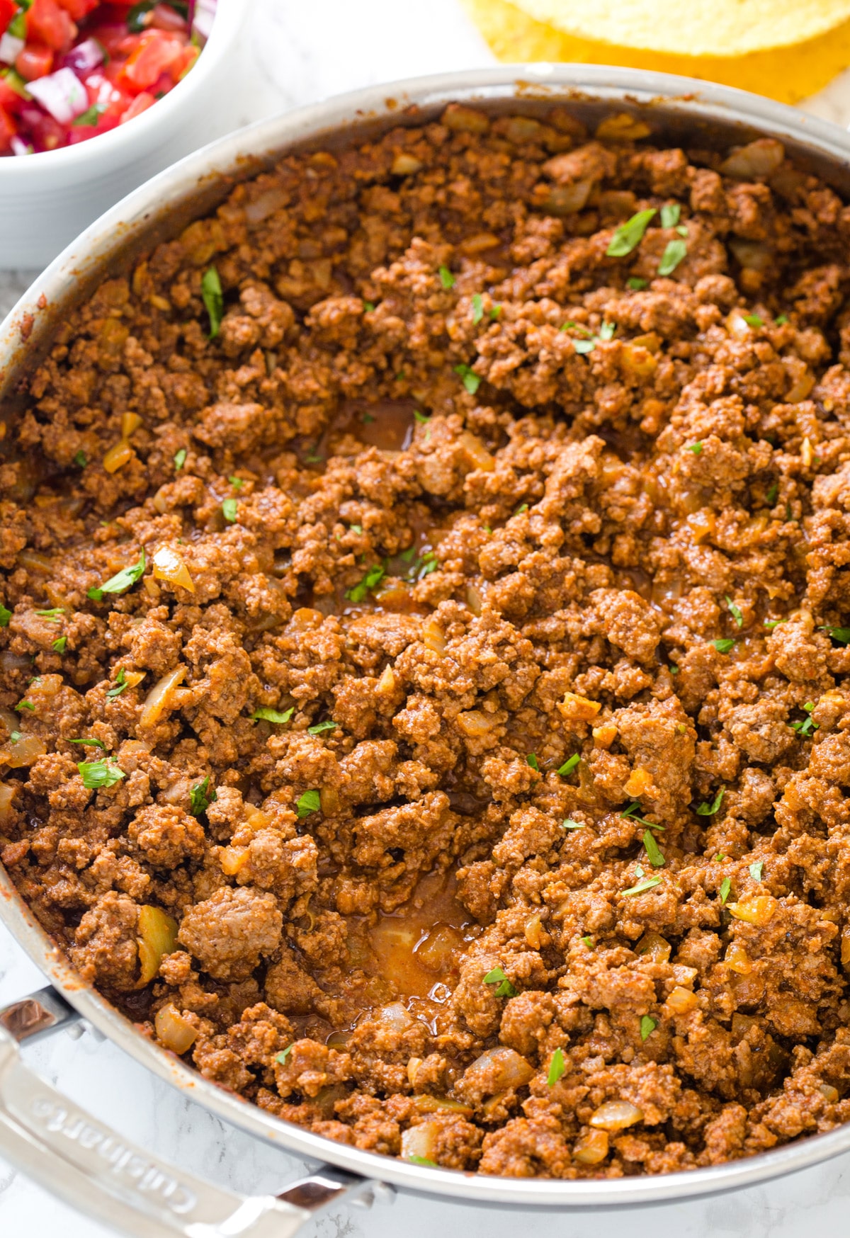 Looking down at taco meat in a stainless steel pan with parsley