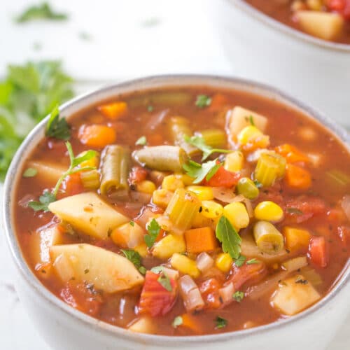 A bowl of soup with vegetables in a tomato broth placed on a white table