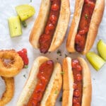 Cooked hot dogs in a bun with pickles and onion rings on a white background