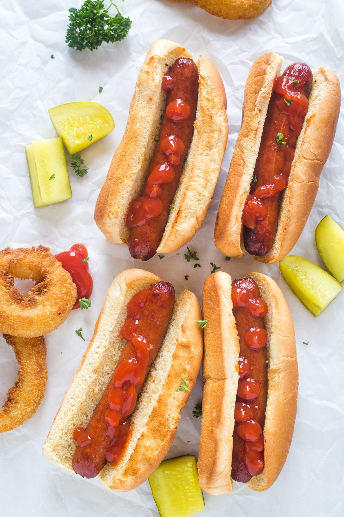 Cooked hot dogs in a bun with pickles and onion rings on a white background