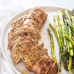 Looking at a cooked and sliced pork tenderloin on a white plate with asparagus