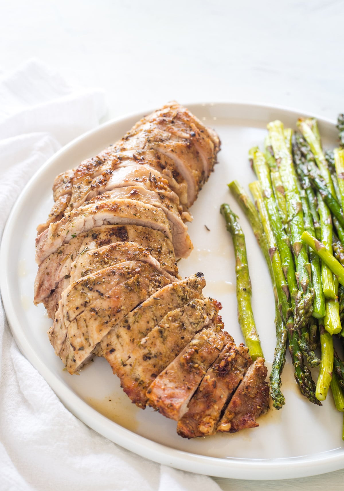 Looking at a cooked and sliced pork tenderloin on a white plate with asparagus