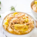 Shredded mississippi chicken in a white bowl served over mashed potatoes